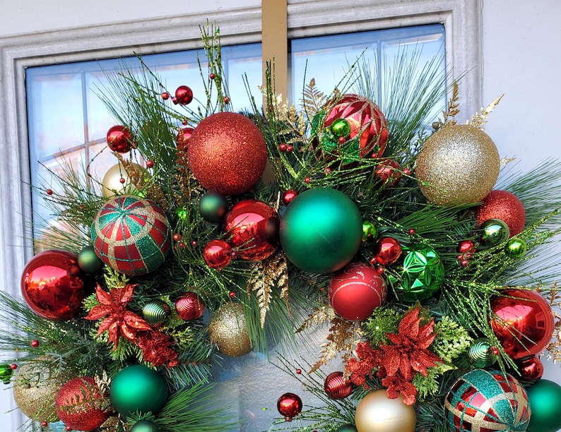 May include: A Christmas wreath with green pine branches, red and gold ornaments, and red poinsettia flowers.