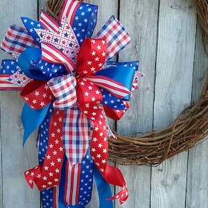 May include: A red, white, and blue patriotic wreath with a grapevine base and a large bow made of various patterned ribbons.