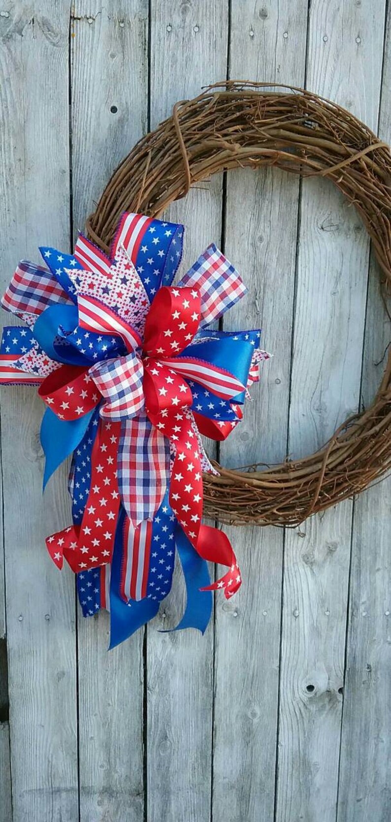 May include: A red, white, and blue patriotic wreath with a grapevine base and a large bow made of various patterned ribbons.