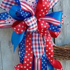 May include: A patriotic wreath bow made with red, white, and blue ribbon. The bow features a variety of patterns, including stars, stripes, and gingham.