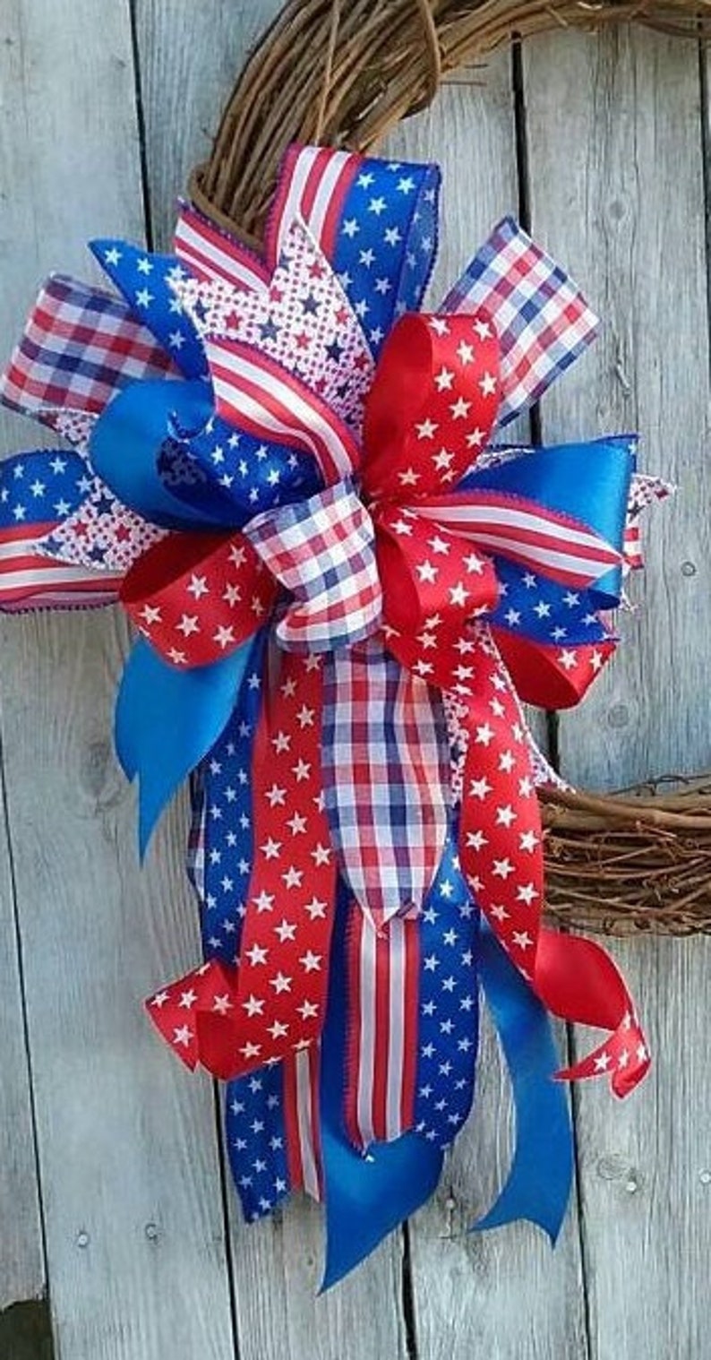 May include: A patriotic wreath bow made with red, white, and blue ribbon. The bow features a variety of patterns, including stars, stripes, and gingham.