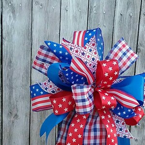May include: A red, white, and blue patriotic bow with stars and stripes, checkered, and solid ribbons, tied around a black lantern.