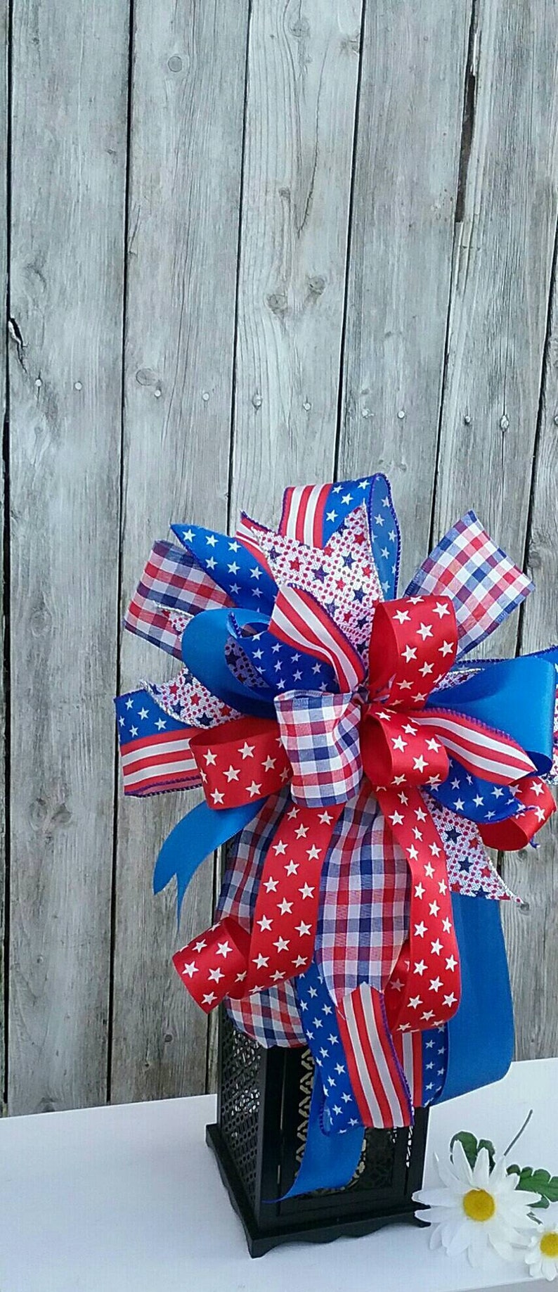 May include: A red, white, and blue patriotic bow with stars and stripes, checkered, and solid ribbons, tied around a black lantern.