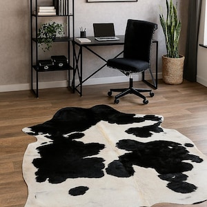 May include: A black and white cowhide rug with irregular black patches on a white background. The rug is on a hardwood floor in a home office setting. A black desk, chair, and shelving unit are also visible.