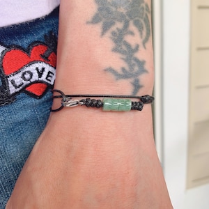 May include: A black string bracelet with a green jade bead and a silver clasp.