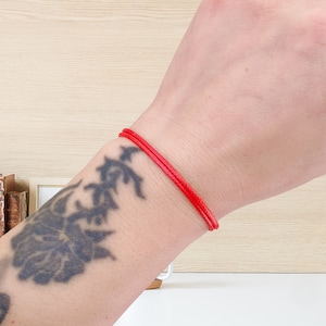 May include: A red string bracelet worn on a person's wrist.