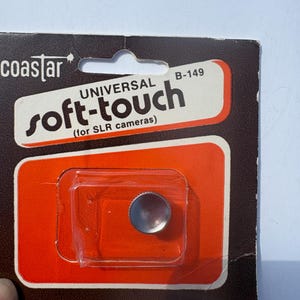 May include: A silver-colored universal soft-touch shutter release button for SLR cameras, model B-149, packaged in a brown and orange cardboard blister pack with the brand name Coastar and the company address in Mount Vernon, New York printed on it.