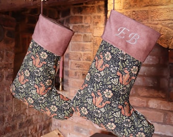 May include: Two Christmas stockings with a floral pattern and pink velvet cuffs. The stockings are hung on a wooden mantel with a string of gold stars. The stocking on the right has the initials "EB" embroidered on the cuff.