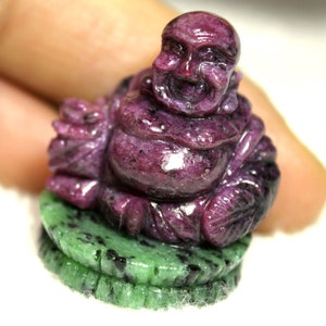 Peut inclure: Une petite figurine sculptée d'un Bouddha rieur en jade violet et vert. Le Bouddha est assis sur une base ronde.