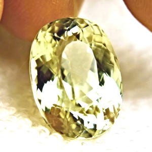 Könnte beinhalten: Ein facettierter, oval geformter Edelstein in einem blassen Gelbgrün. Der Stein verfügt über einen Brillantschliff mit zahlreichen dreieckigen und rautenförmigen Facetten, die das Licht reflektieren und ein helles, durchscheinendes Aussehen erzeugen.