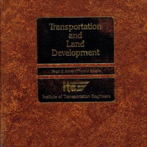 May include: A hardcover book titled "Transportation and Land Development" with a brown textured cover. The title is in gold lettering on a black rectangular label. The book is published by the Institute of Transportation Engineers.