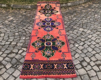 Könnte beinhalten: Ein langer, schmaler Teppich mit traditionellem marokkanischem Design. Der Teppich ist in einem leuchtenden Korallenrot mit komplizierten blauen, grünen und schwarzen Mustern gehalten. Der Teppich hat einen Fransenrand.