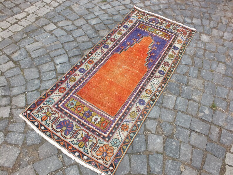 May include: A vintage orange prayer rug with a traditional floral design and a blue and white prayer niche. The rug has a white fringe border.