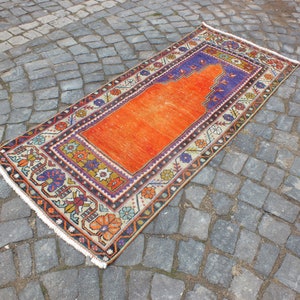 May include: A traditional orange and cream prayer rug with a blue and purple border. The rug has a central prayer niche and intricate floral designs.