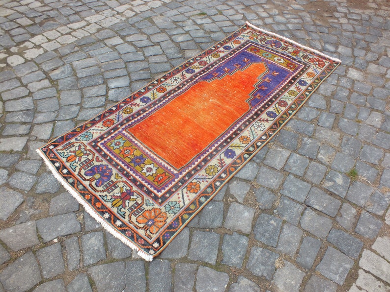 May include: A traditional orange and cream prayer rug with a blue and purple border. The rug has a central prayer niche and intricate floral designs.