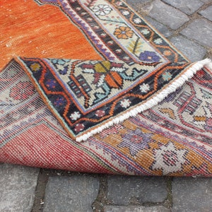 May include: A vintage orange and cream rug with a geometric pattern and fringe. The rug is folded in half, showing the back side with a similar pattern.