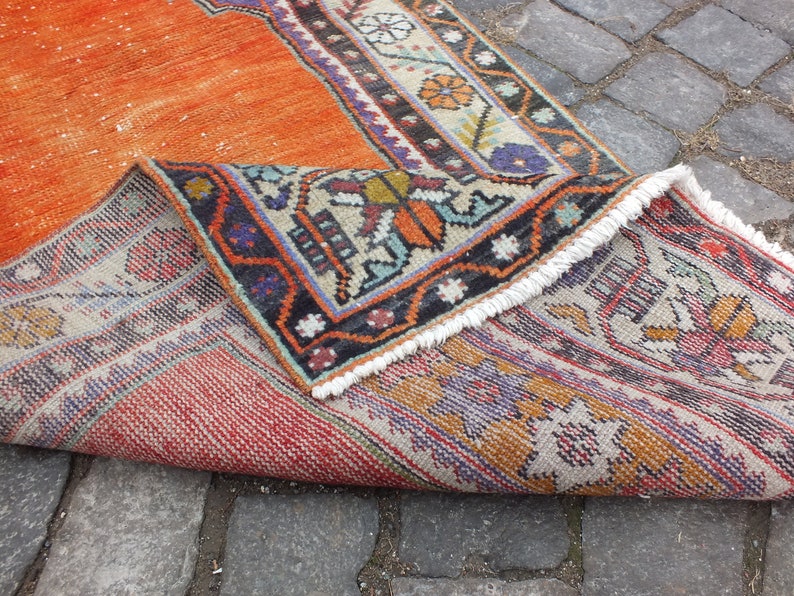 May include: A vintage orange and cream rug with a geometric pattern and fringe. The rug is folded in half, showing the back side with a similar pattern.