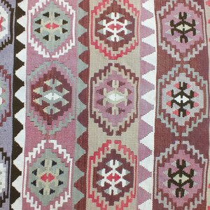 May include: A woven rug with a geometric pattern in shades of purple, red, brown, and beige. The design features repeating diamond and hexagonal shapes, creating a symmetrical and textured appearance. The rug's design is a traditional style.