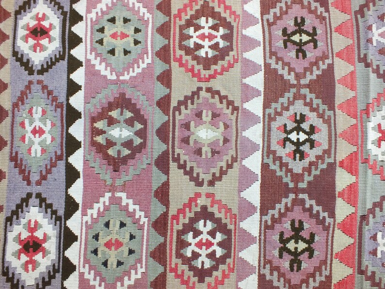 May include: A woven rug with a geometric pattern in shades of purple, red, brown, and beige. The design features repeating diamond and hexagonal shapes, creating a symmetrical and textured appearance. The rug's design is a traditional style.
