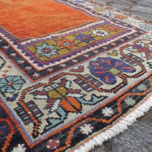 May include: A vintage orange and cream rug with a colorful geometric pattern and fringe. The rug has a traditional design with floral motifs and a black border.