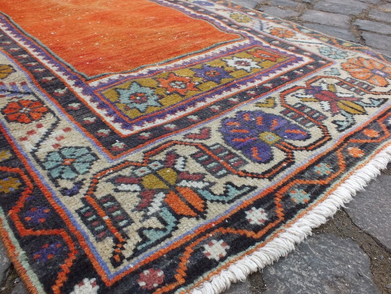 May include: A vintage orange and cream rug with a colorful geometric pattern and fringe. The rug has a traditional design with floral motifs and a black border.