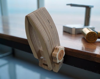 May include: A wooden clamp with a knob featuring a mountain logo. The clamp is made of light brown wood with a natural wood grain pattern. The knob is made of a lighter wood and has a star-shaped design.