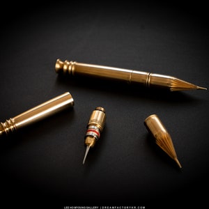 May include: A set of four gold-colored metal pen parts, including a pen body, a nib, a cap, and a cartridge. The pen parts are arranged on a black surface.