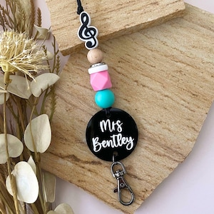 May include: A black and white music note charm with a black and white name tag that reads "Mrs. Bentley" on a black lanyard with pink, turquoise, and white beads.