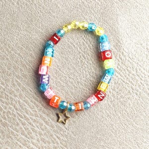 May include: A circular bracelet made of multicolored translucent faceted beads and square letter beads spelling out I KNEW IT. The bracelet features a small, gold-toned metal star charm dangling from the bottom, interspersed with blue, yellow, pink, and red beads.