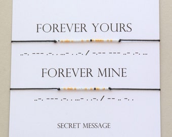May include: Two black string bracelets with white and gold beads spelling out "FOREVER YOURS" and "FOREVER MINE" in Morse code. The bracelets are displayed on a white card with the text "Morse code Bracelet" and "SECRET MESSAGE".