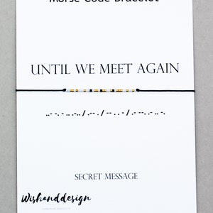 May include: A black string bracelet with gold and white beads spelling out the message "UNTIL WE MEET AGAIN" in Morse code. The message is written below the bracelet.