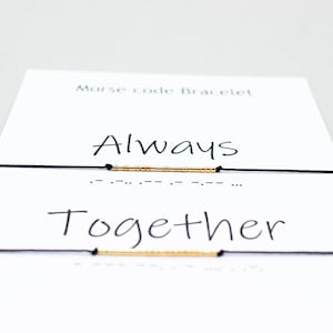 May include: Two black string bracelets with gold beads spelling out the words "Always" and "Together" in Morse code. The bracelets are displayed on a white card with the words "Morse code bracelet" at the top.