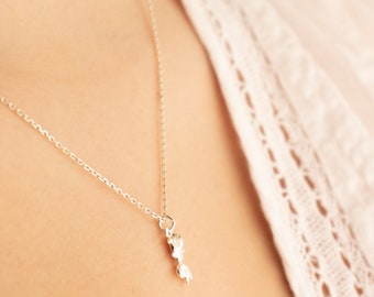 May include: A silver chain necklace with a small, abstract pendant. The pendant is a simple, organic shape.