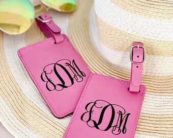 May include: Two pink leather luggage tags with black monogrammed initials "DM" on a straw hat.
