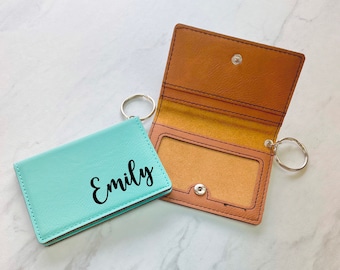 May include: A turquoise leather key chain with a silver key ring and a brown leather card holder with a clear plastic window. The key chain has the name "Emily" embossed on it.