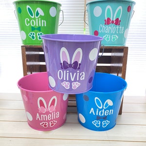 May include: Five colorful metal buckets with bunny ears and polka dots. Each bucket has a name on it: Colin, Charlotte, Olivia, Amelia, and Aiden.