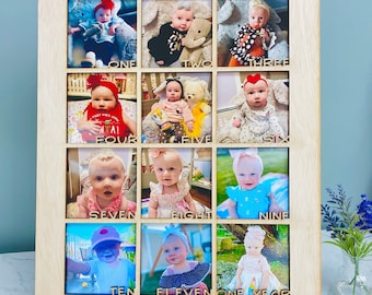 May include: A wooden photo frame with twelve openings, each displaying a baby's monthly photo. The frame is engraved with "Lily Grace" at the top and month numbers below each photo. The frame is made of light-colored wood.