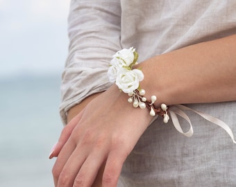 May include: A white floral bracelet with pearl accents and a white ribbon.