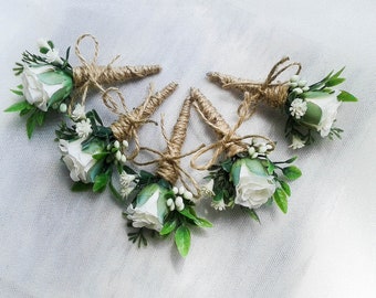 Puede incluir: Cinco boutonnières de rosas blancas con detalles de vegetación y cuerda de yute.