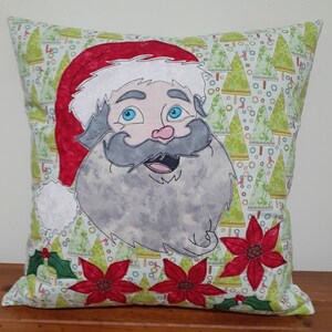 May include: A green and white pillow with a festive Christmas design featuring a smiling Santa Claus with a red hat and white beard, surrounded by poinsettia flowers and holly.