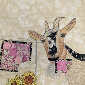 May include: A whimsical embroidered artwork featuring a goat with a floral design, surrounded by sunflowers and other floral elements. The artwork is on a beige fabric background.