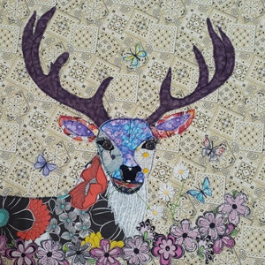 May include: A colorful patchwork deer with large antlers, surrounded by a border of flowers and butterflies. The deer's face is detailed with embroidered eyes and a nose.