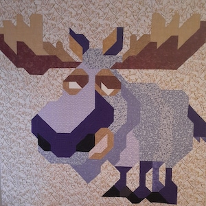 May include: A purple and brown patchwork quilt depicting a cartoon moose with a surprised expression. The moose has large antlers and is standing on a white background with a brown floral pattern.