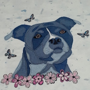 May include: A denim-textured dog portrait with a white snout and brown eyes. The dog is surrounded by three butterflies and a garland of pink and white flowers. The background is light blue with darker blue paint splatters.