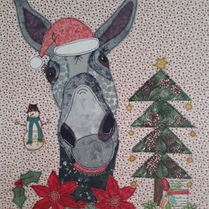 May include: A gray donkey wearing a red Santa hat with white trim, standing in front of a green Christmas tree with brown pine cones and gold ornaments. There is a snowman with a blue scarf to the left of the donkey and a red poinsettia flower to the right.