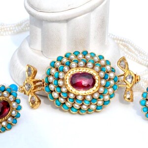 Puede incluir: Un collar de oro con un colgante de turquesa y perlas, y pendientes a juego. El colgante presenta una piedra preciosa roja en el centro.
