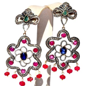 Puede incluir: Pendientes de plata con un diseño en forma de estrella, con un zafiro azul, rubíes rojos y pequeños diamantes. Los pendientes tienen un diseño colgante con cuentas de rubí rojo.