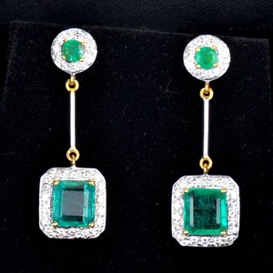 May include: A pair of emerald and diamond drop earrings. The earrings feature a square emerald surrounded by a halo of diamonds, and a smaller round emerald at the top of the earring.