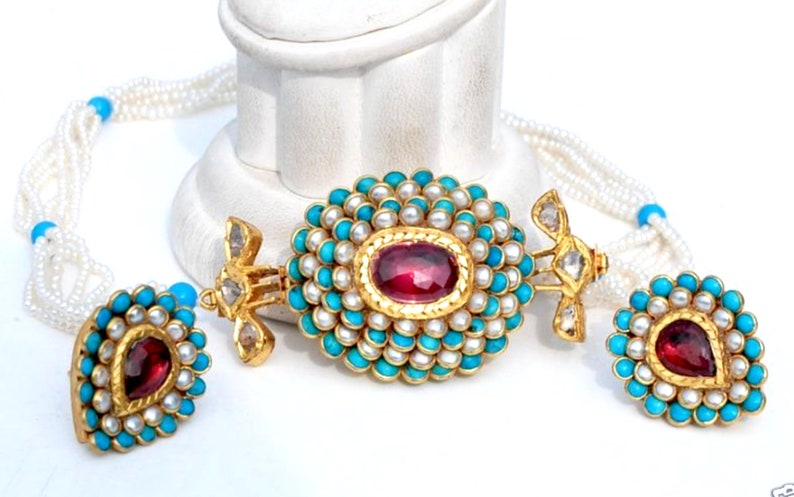 Puede incluir: Un collar de oro con un colgante de turquesa y perlas, y pendientes a juego. El colgante presenta una piedra preciosa roja en el centro.