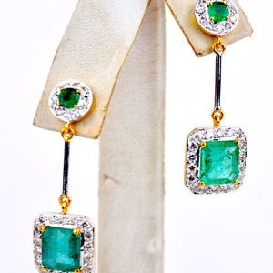 May include: A pair of gold drop earrings featuring emerald green gemstones surrounded by a halo of smaller diamonds. The earrings have a square-shaped emerald gemstone at the bottom.